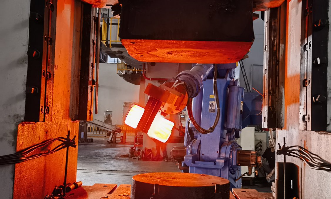 Robotic manipulator gripping a red-hot billet in front of the forging press